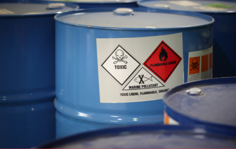 The image shows toxic substances in blue barrels in a factory.