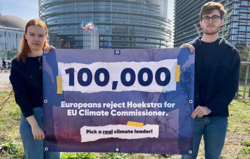 Two people hold a banner in front of the European Parliament in Strasbourg saying "100,000 Europeans reject Hoekstra for EU Climate Commissioner