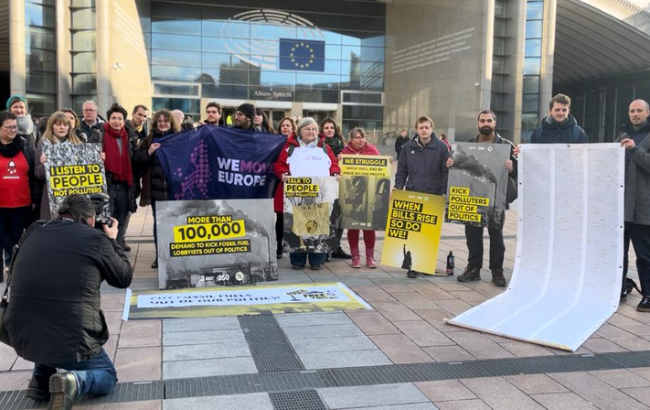 Group of peopole standing in front of the European Parliament, holding the signs from the petition for Fossil Free Politics