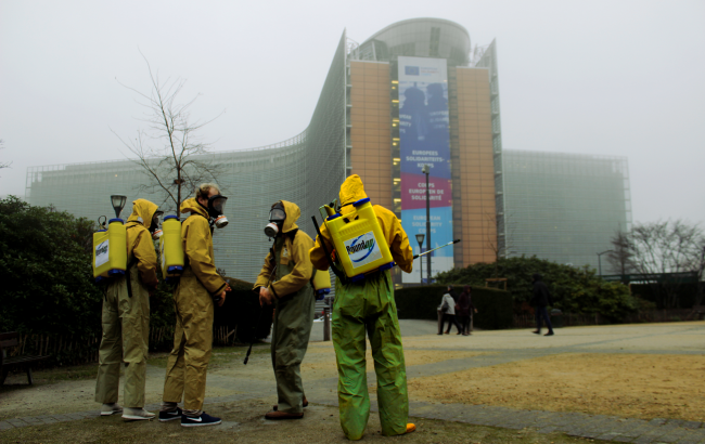 Four people wearing yellow overalls and "Roundup" pesticide tanks stand in front of the European Commission