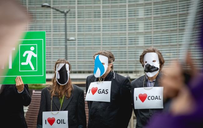 Rally in front of the EU Commission. Three activists wear white masks and signs saying "I love oil", "I love gas" and "I love coal".