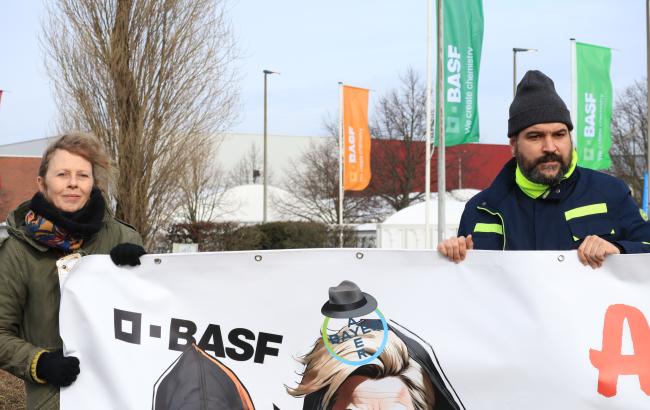 CEO's researchers and campaigners Nina and Joao holding a banner outside BASF chemical plant in Antwerp